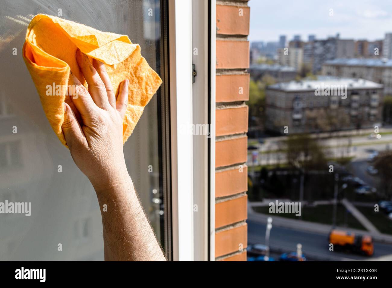male hand wipes open window with rag in high-rise city house on sunny ...
