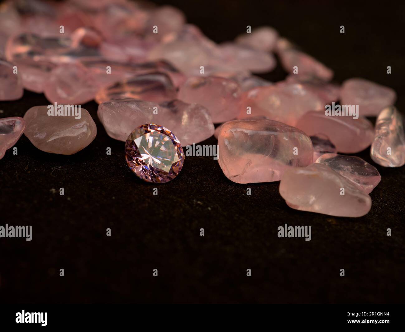 Round cut pink colored diamond and tumbled crystals on black background Stock Photo