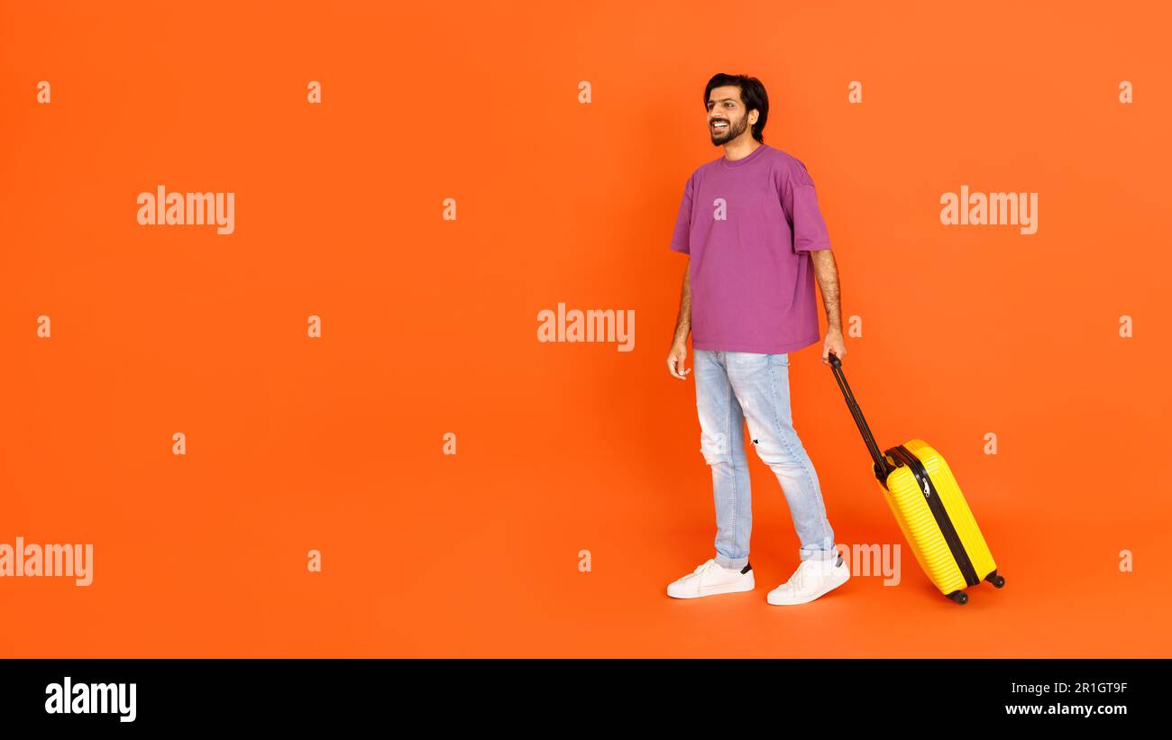 Happy young eastern man with luggage looking at empty space Stock Photo