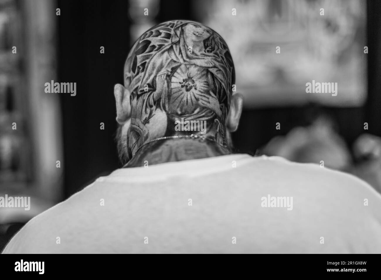 A black and white image of a rear view of a bald man with a tattoo on his skull. Stock Photo