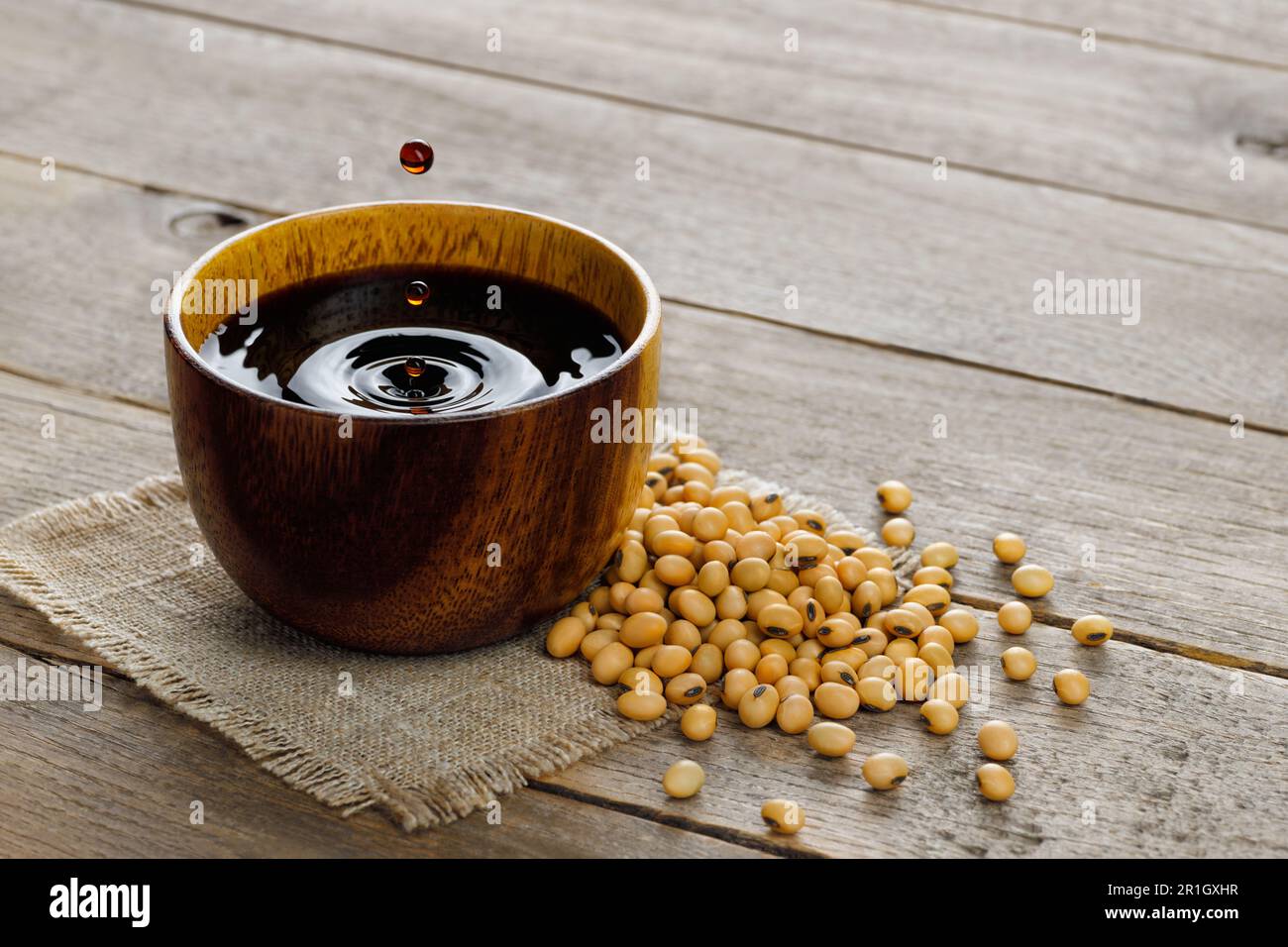 soy sauce in bowl with falling drops and dry soybeans on table Stock Photo
