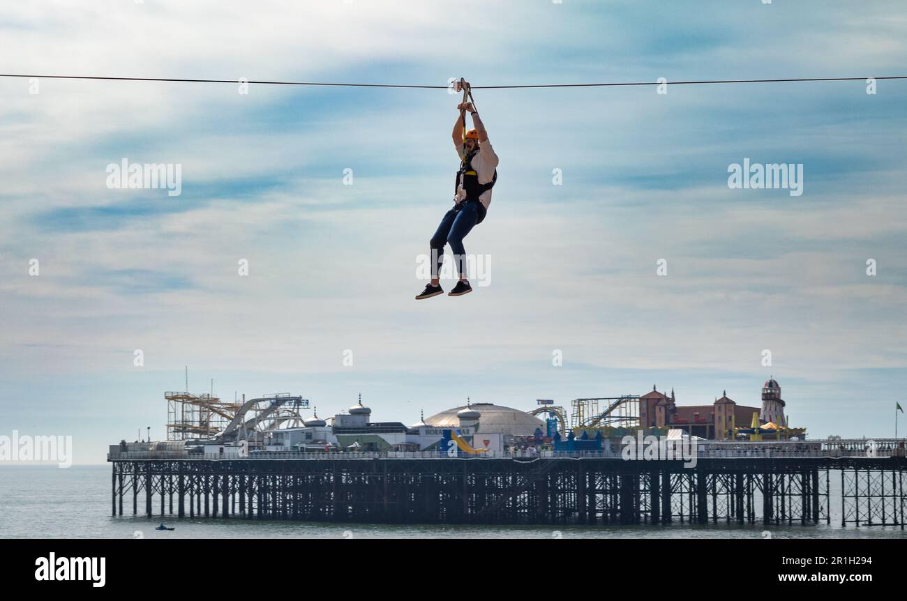 A man in a harness and wearing a helmet travels on a zip wire across Brighton beach in front of the famous Brighton Pier and its funfair. Brighton, a Stock Photo