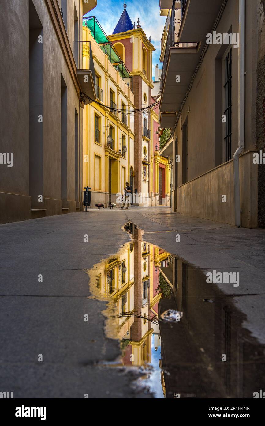 Málaga, Spain - Nov 25 2022: Old town of Málaga with the tower of the Cathedral in the background, reflected in a puddle Stock Photo