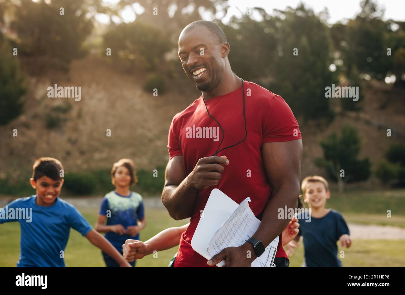 Coach having a fun training session with kids in a school. PE teacher coaching a group of elementary school children. Sports education in primary scho Stock Photo