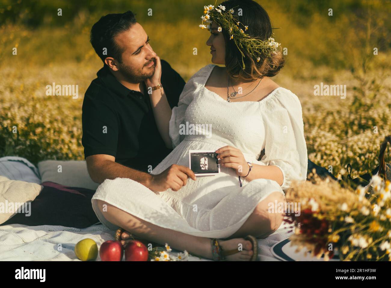 Sitting on a white picnic blanket, a pregnant woman with a daisy crown