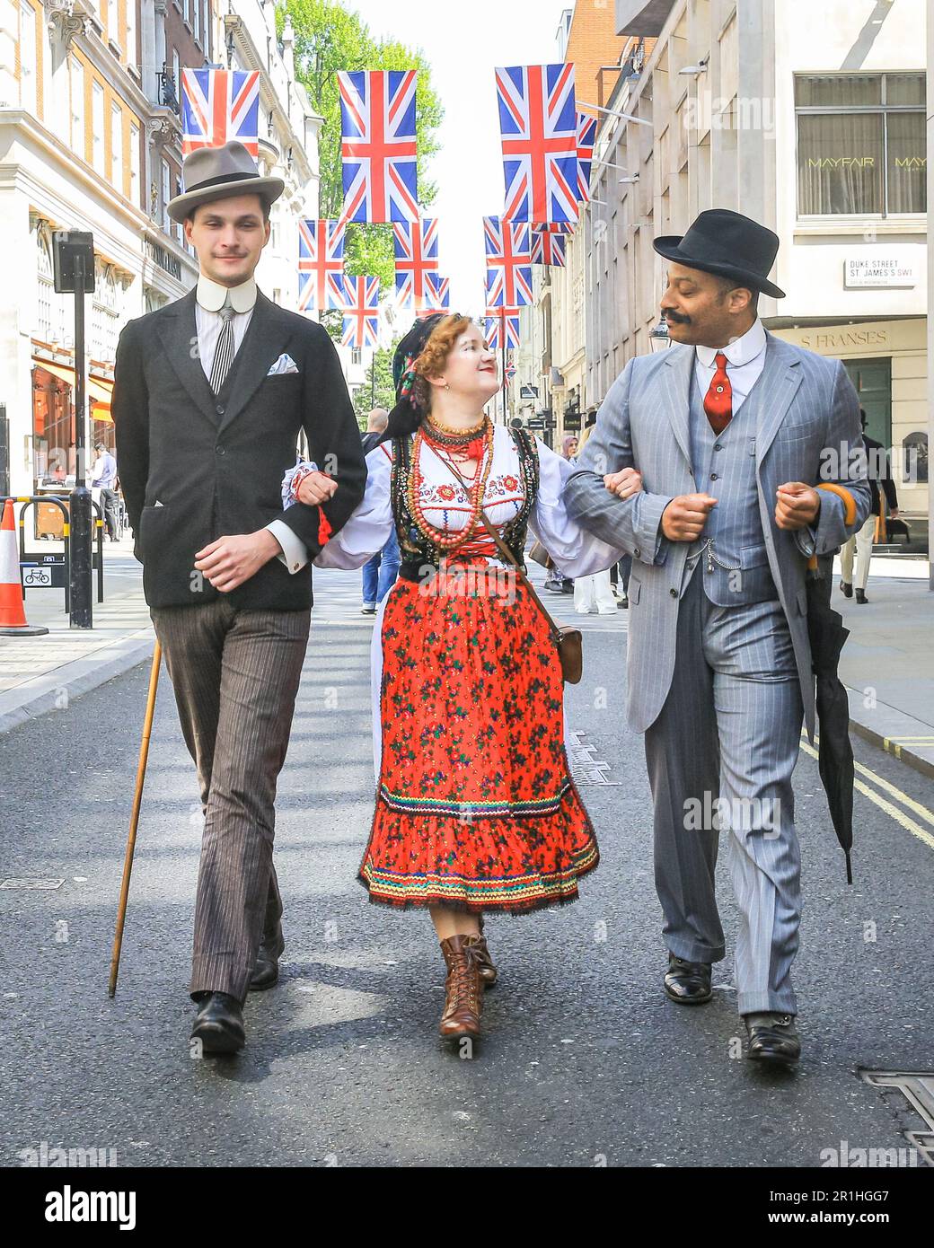 London, UK. 14th May, 2023. Two chaps gentlemanly walk with a young lady in Polish folk dress along Jermyn Street. The annual Grand Flaneur Walk sees chaps and chapettes, dandies and quaintrelle in impeccable tailoring and style flanning and sauntering without purpose around St James' and surrounding areas of London. The walk always starts at the statue of socialite dandy Beau Brummell and slowly makes its way around the area. Credit: Imageplotter/Alamy Live News Stock Photo