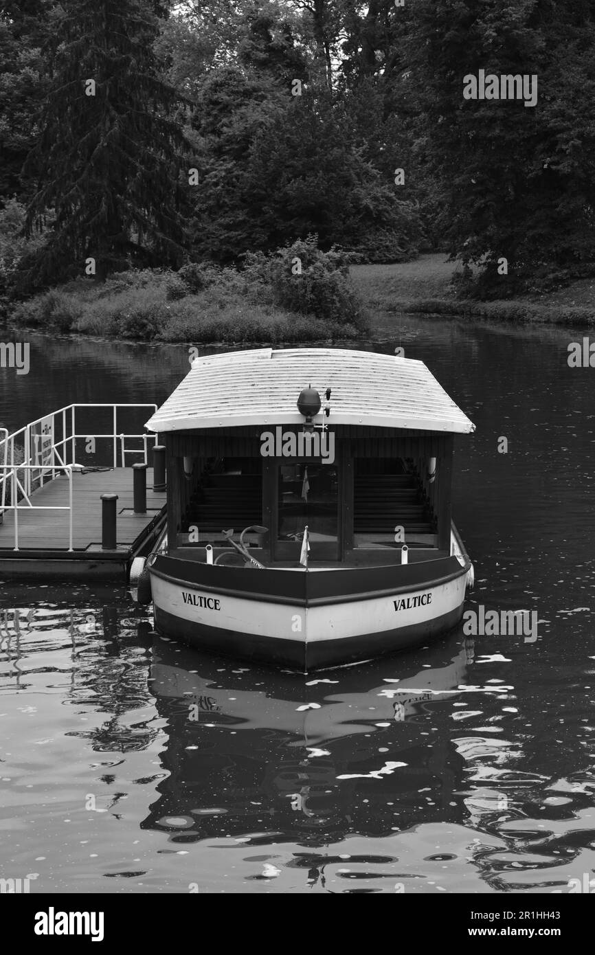 A greyscale of a tranquil scene of a small boat named "Valtice" docked at a wooden pier Stock Photo