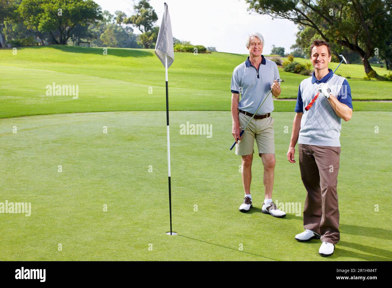 Father and son playing golf. Full length of smiling father and son standing on the putting green with golf clubs. Stock Photo