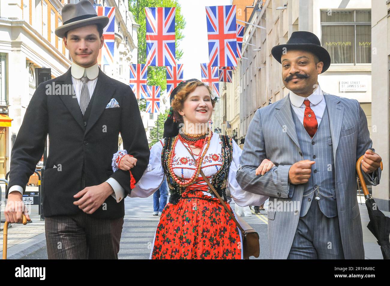 London, UK. 14th May, 2023. Two chaps gentlemanly walk with a young lady in Polish folk dress along Jermyn Street. The annual Grand Flaneur Walk sees chaps and chapettes, dandies and quaintrelle in impeccable tailoring and style flanning and sauntering without purpose around St James' and surrounding areas of London. The walk always starts at the statue of socialite dandy Beau Brummell and slowly makes its way around the area. Credit: Imageplotter/Alamy Live News Stock Photo