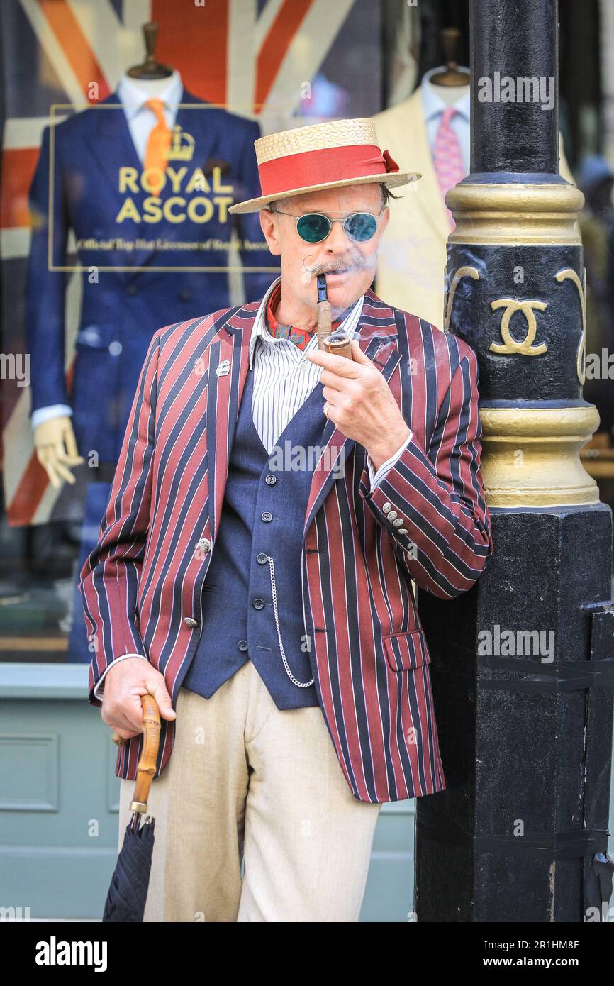 London, UK. 14th May, 2023. A chap enjoys his pipe. The annual Grand Flaneur Walk sees chaps and chapettes, dandies and quaintrelle in impeccable tailoring and style flanning and sauntering without purpose around St James' and surrounding areas of London. The walk always starts at the statue of socialite dandy Beau Brummell and slowly makes its way around the area. Credit: Imageplotter/Alamy Live News Stock Photo