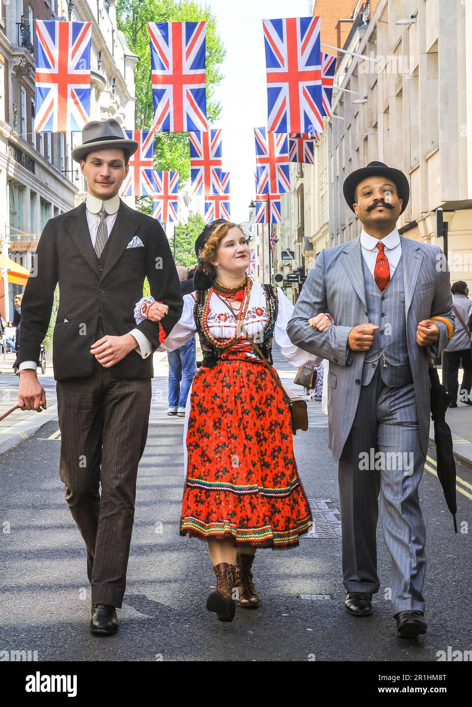 London, UK. 14th May, 2023. Two chaps gentlemanly walk with a young lady in Polish folk dress along Jermyn Street. The annual Grand Flaneur Walk sees chaps and chapettes, dandies and quaintrelle in impeccable tailoring and style flanning and sauntering without purpose around St James' and surrounding areas of London. The walk always starts at the statue of socialite dandy Beau Brummell and slowly makes its way around the area. Credit: Imageplotter/Alamy Live News Stock Photo