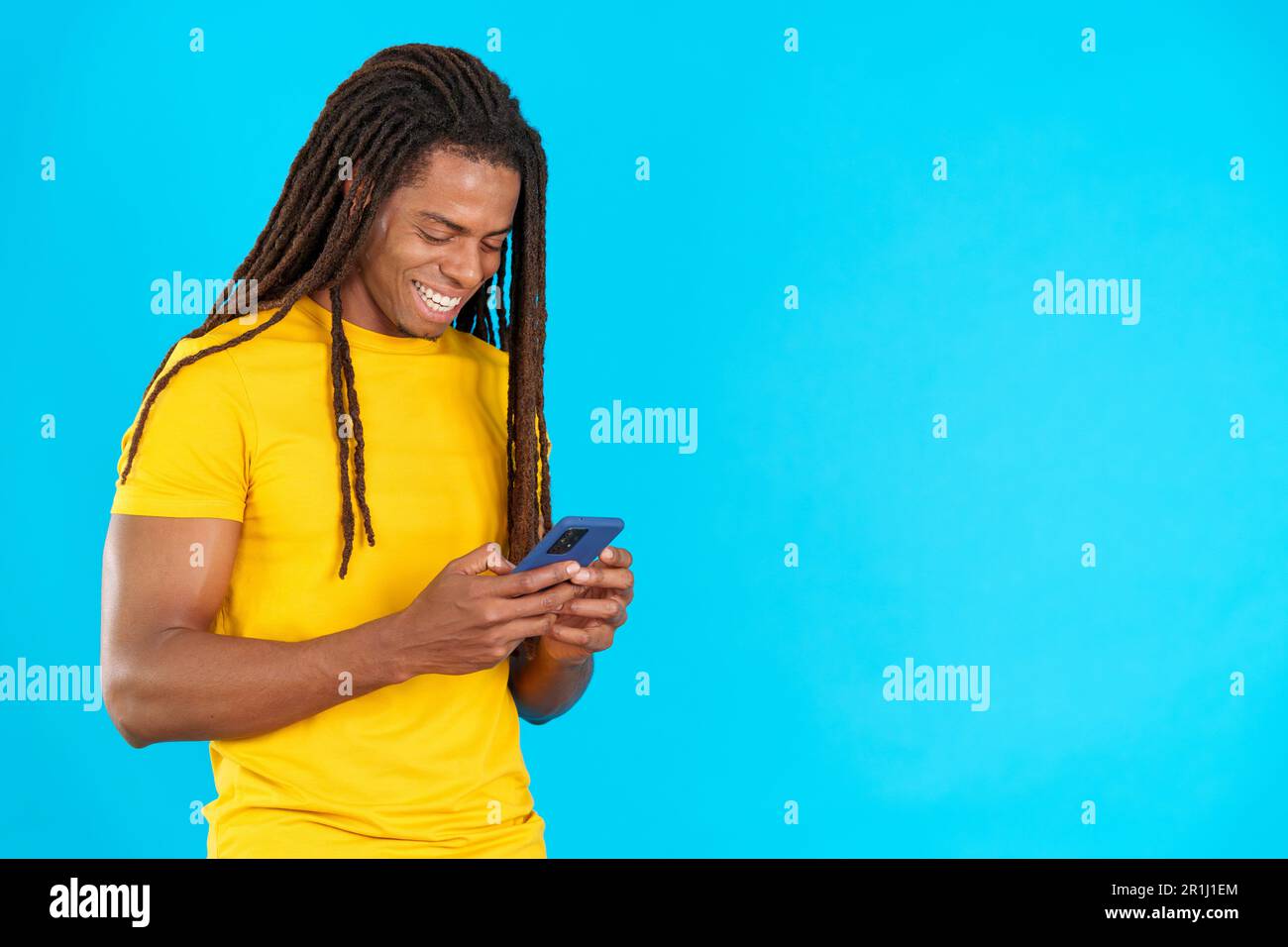 Happy latin man with dreadlocks smiling while using the mobile Stock Photo