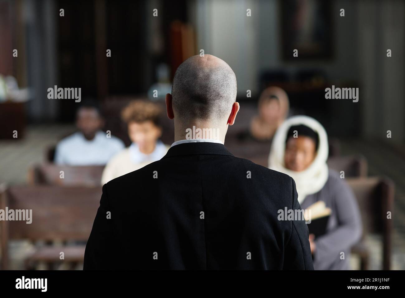 Rear view of pastor in black suit talking to believers while tehy sitting on bench in church Stock Photo