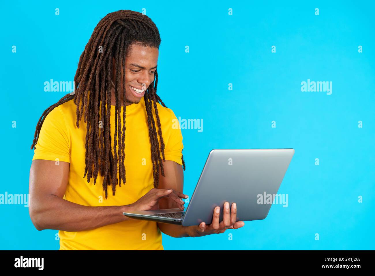 Latin man with dreadlocks smiling while using a laptop Stock Photo