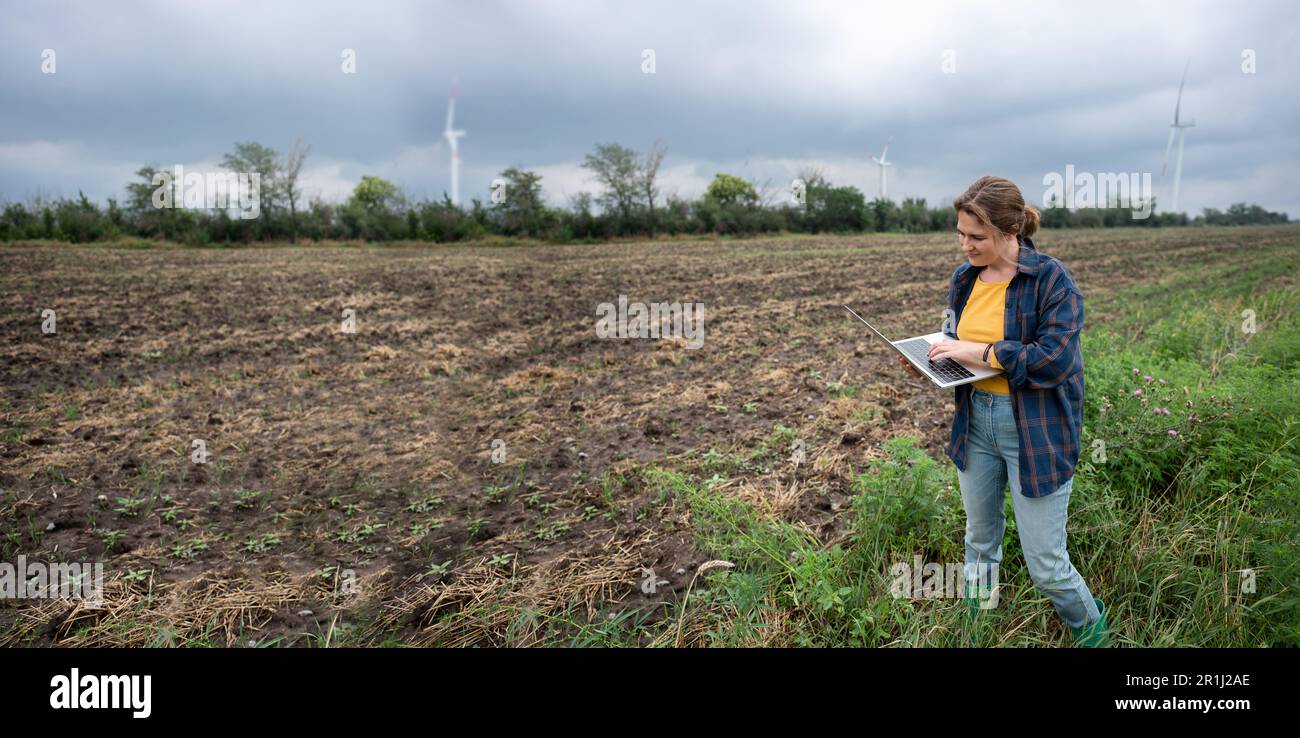 Farmer with laptop on the field. Wind turbines on a horizon. Smart sustainable farming and agriculture digitalization. High quality photo Stock Photo