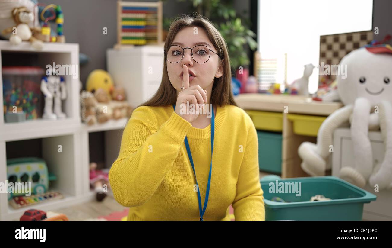 Young blonde woman preschool teacher asking for silence at kindergarten Stock Photo