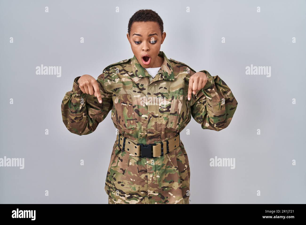 Beautiful african american woman wearing camouflage army uniform pointing down with fingers showing advertisement, surprised face and open mouth Stock Photo