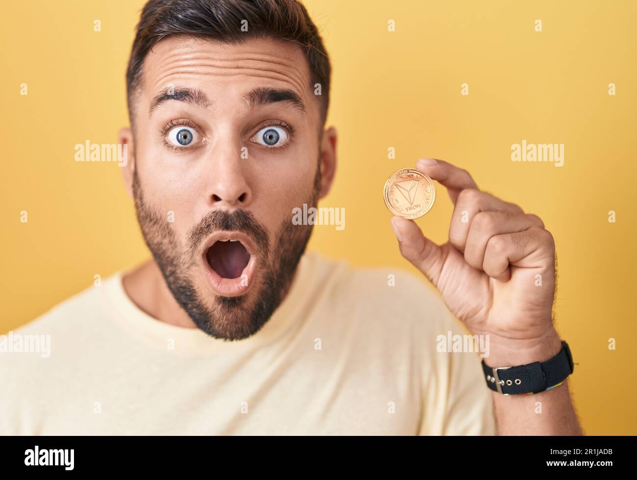 Handsome hispanic man holding tron cryptocurrency coin scared and amazed  with open mouth for surprise, disbelief face Stock Photo - Alamy