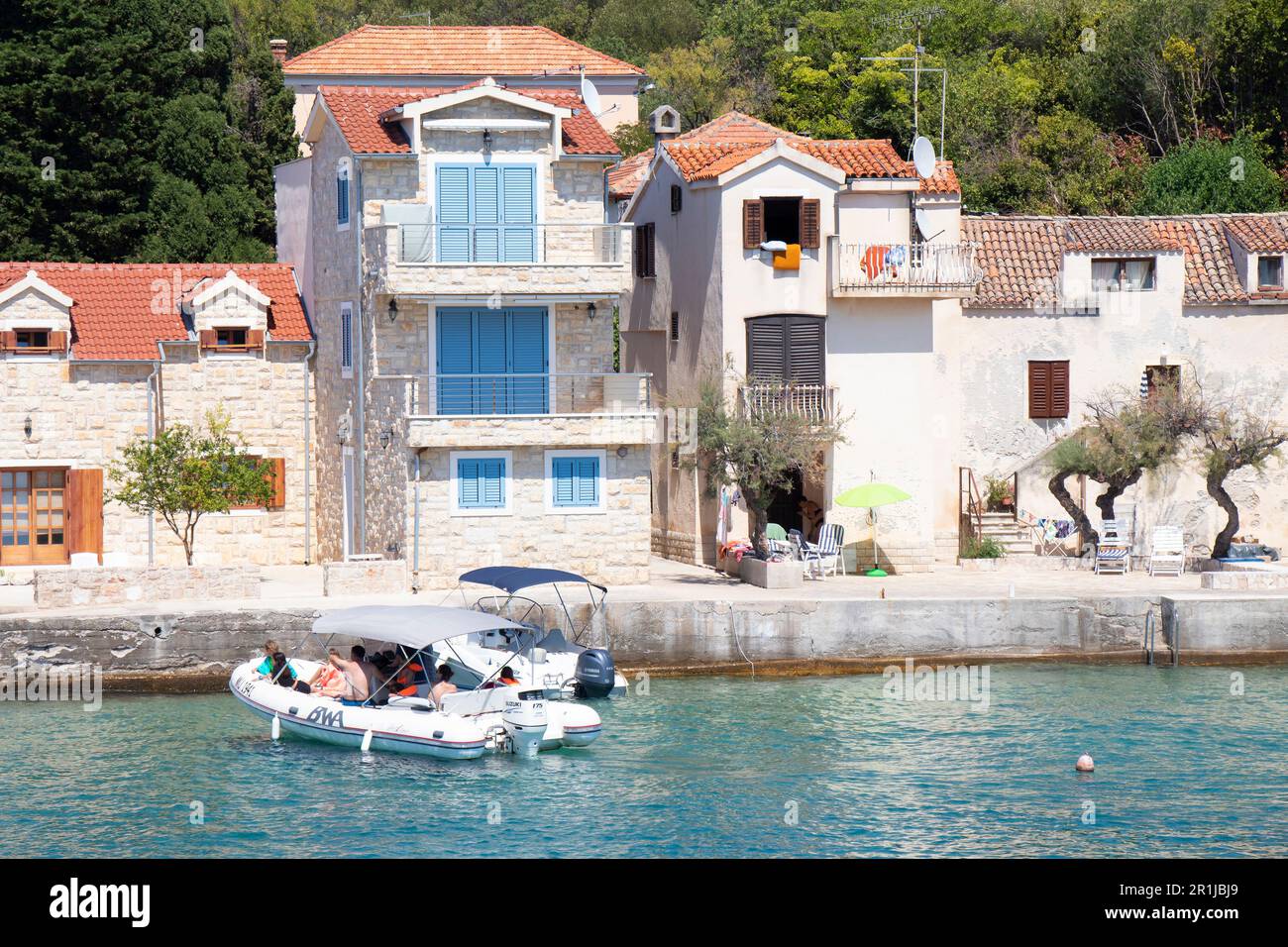 Prvic Luka, Croatia - July 22, 2022: Stone houses by the sea and a rubber boat arriving to the dock Stock Photo