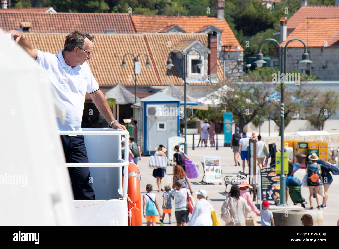 Zlarin island, Croatia - July 22, 2022: People leaving the pier, and a man working on a Jadrolinija ferry watching from the deck Stock Photo