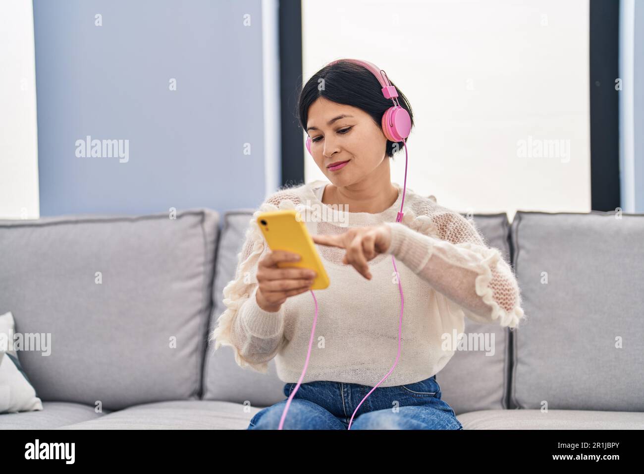 Young chinese woman listening to music sitting on sofa at home Stock ...