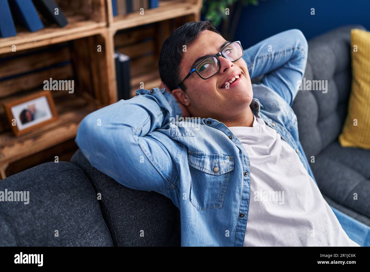 Down syndrome man relaxed with hands on head sitting on sofa at home Stock Photo