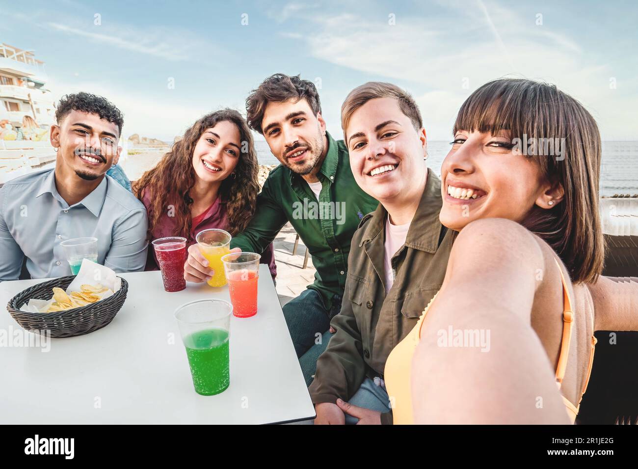 A multiracial group of friends takes a selfie at an outdoor bar table ...