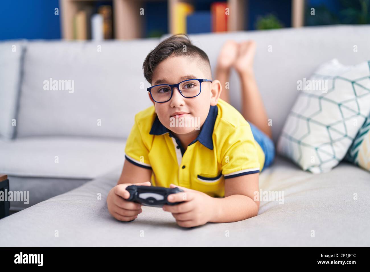 Kid Using Controller Young hispanic kid playing video game holding controller on the sofa ...