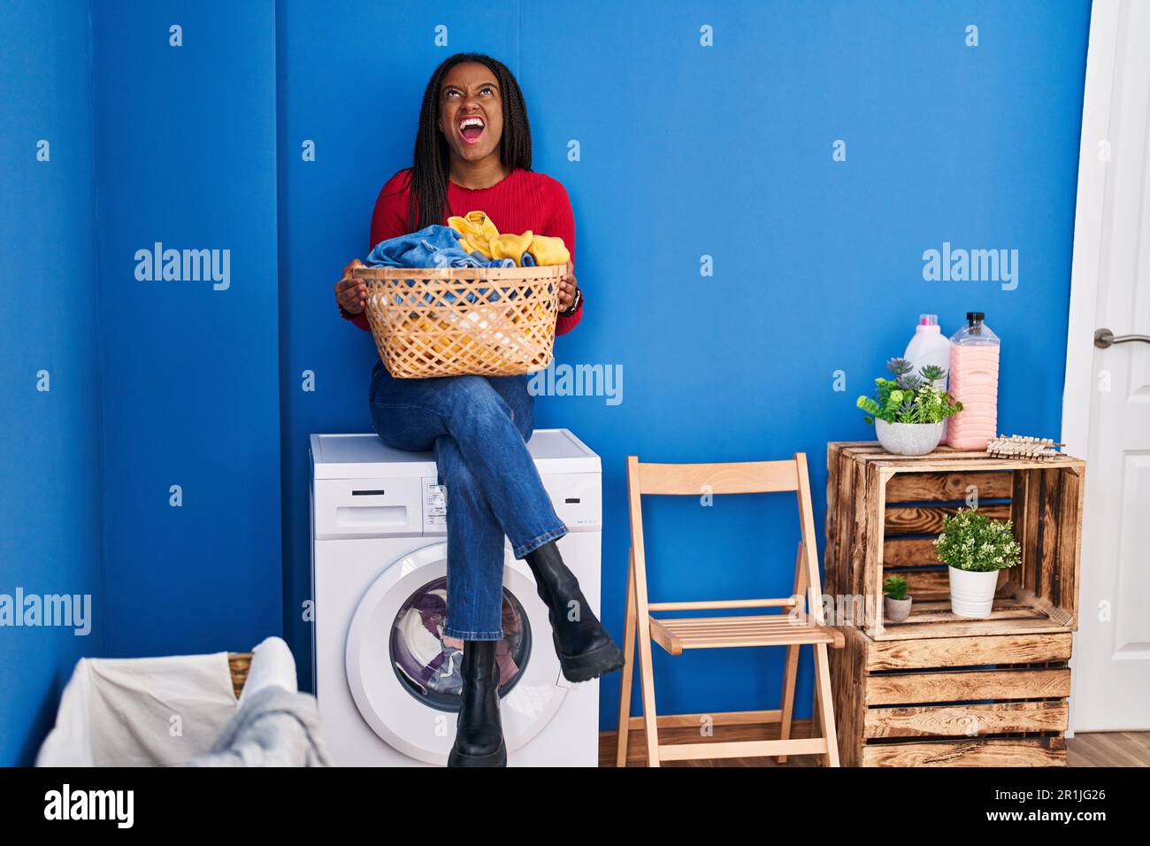 Young african american with braids holding laundry basket sitting on ...