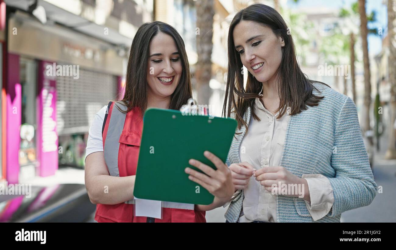 Two women having survey interview writing on clipboard at street Stock Photo