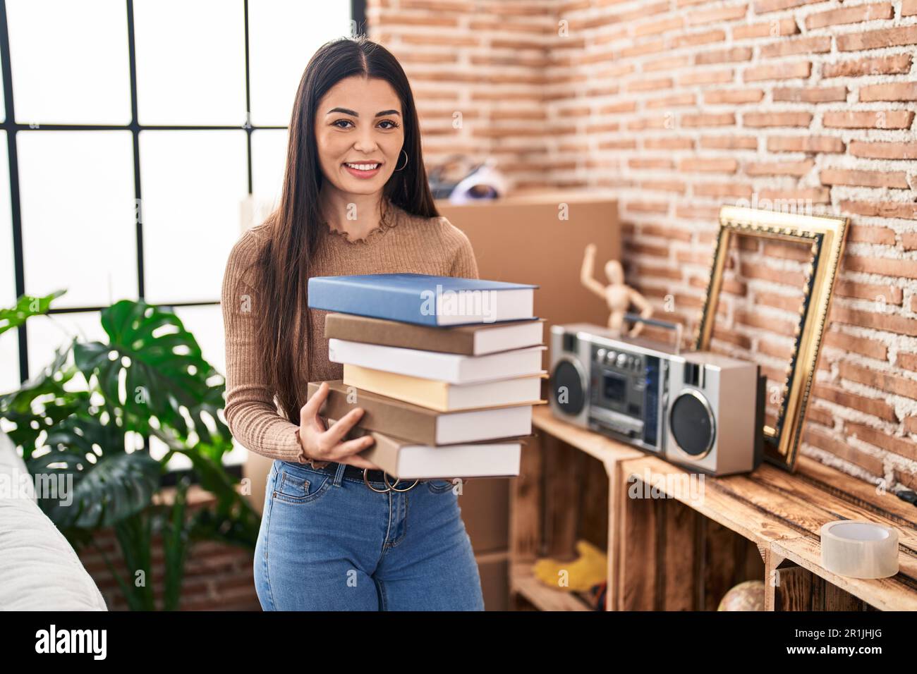 Young woman holding books at home smiling with a happy and cool smile ...