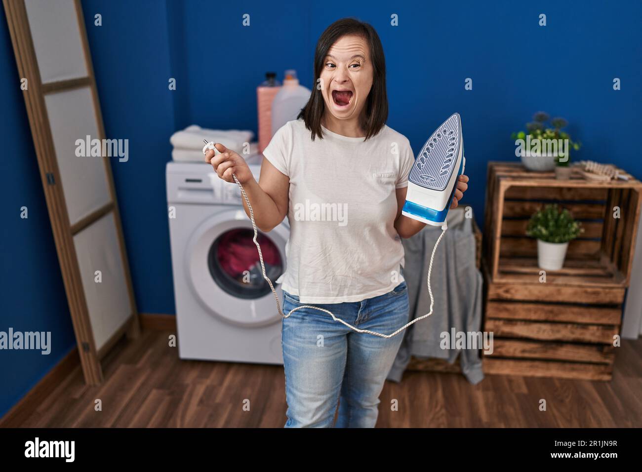 Hispanic girl with down syndrome ironing clothes at home angry and mad screaming frustrated and furious, shouting with anger. rage and aggressive conc Stock Photo