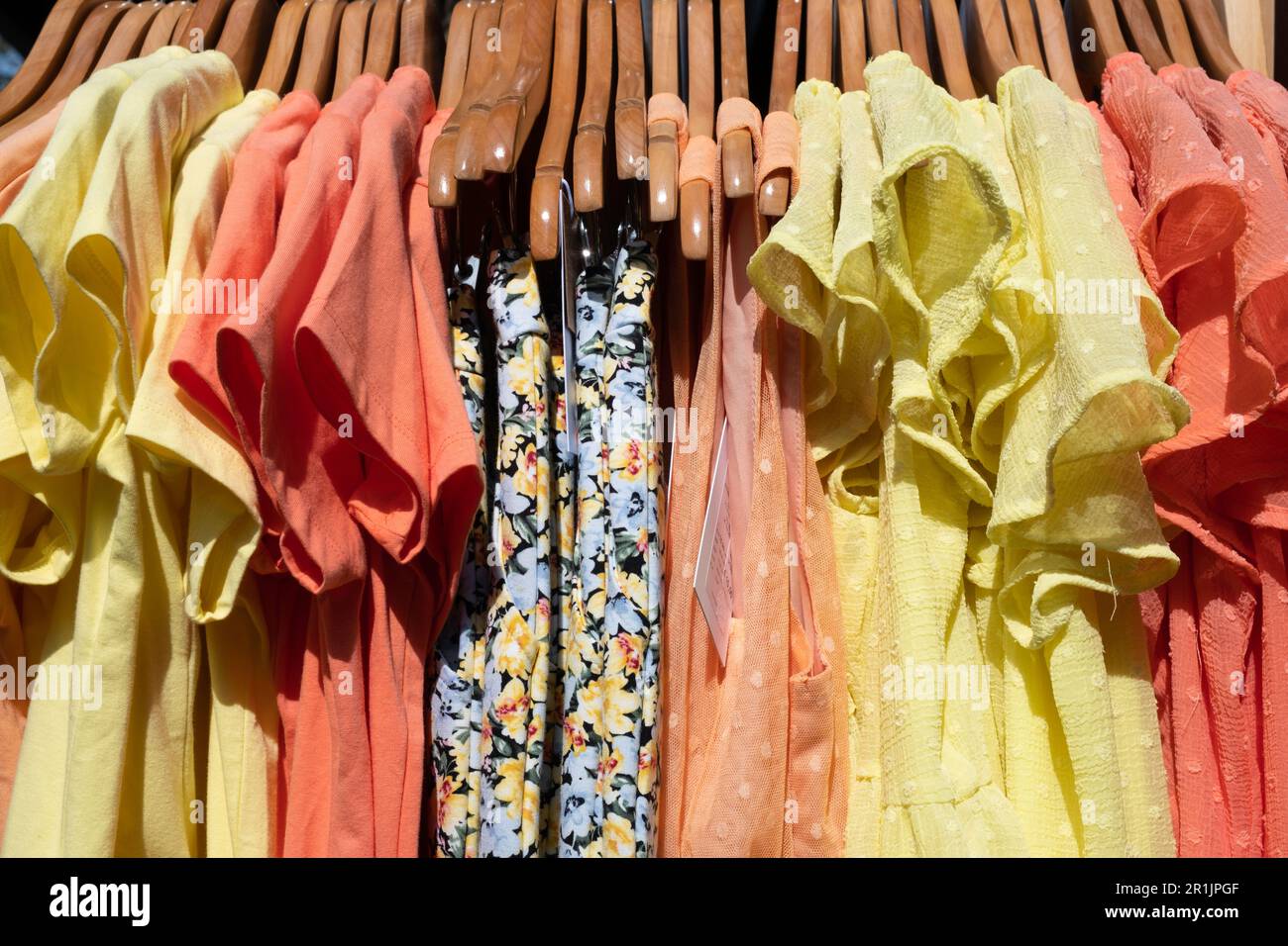 Cheap colorful summer dresses hang back to back in the sun on wooden