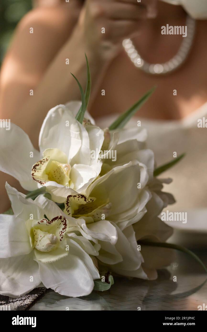 Wedding bouquet of the bride. The bride in a white necklace sits at the table and drinks coffee. The image of the bride is blurry Stock Photo