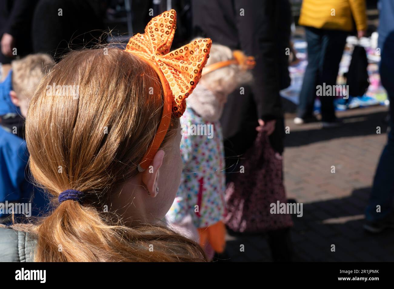 Girl with orange bow in her hair watches people walk by on King's Day ('Koningsdag'), the birthday of King Willem-Alexander of the Netherlands Stock Photo