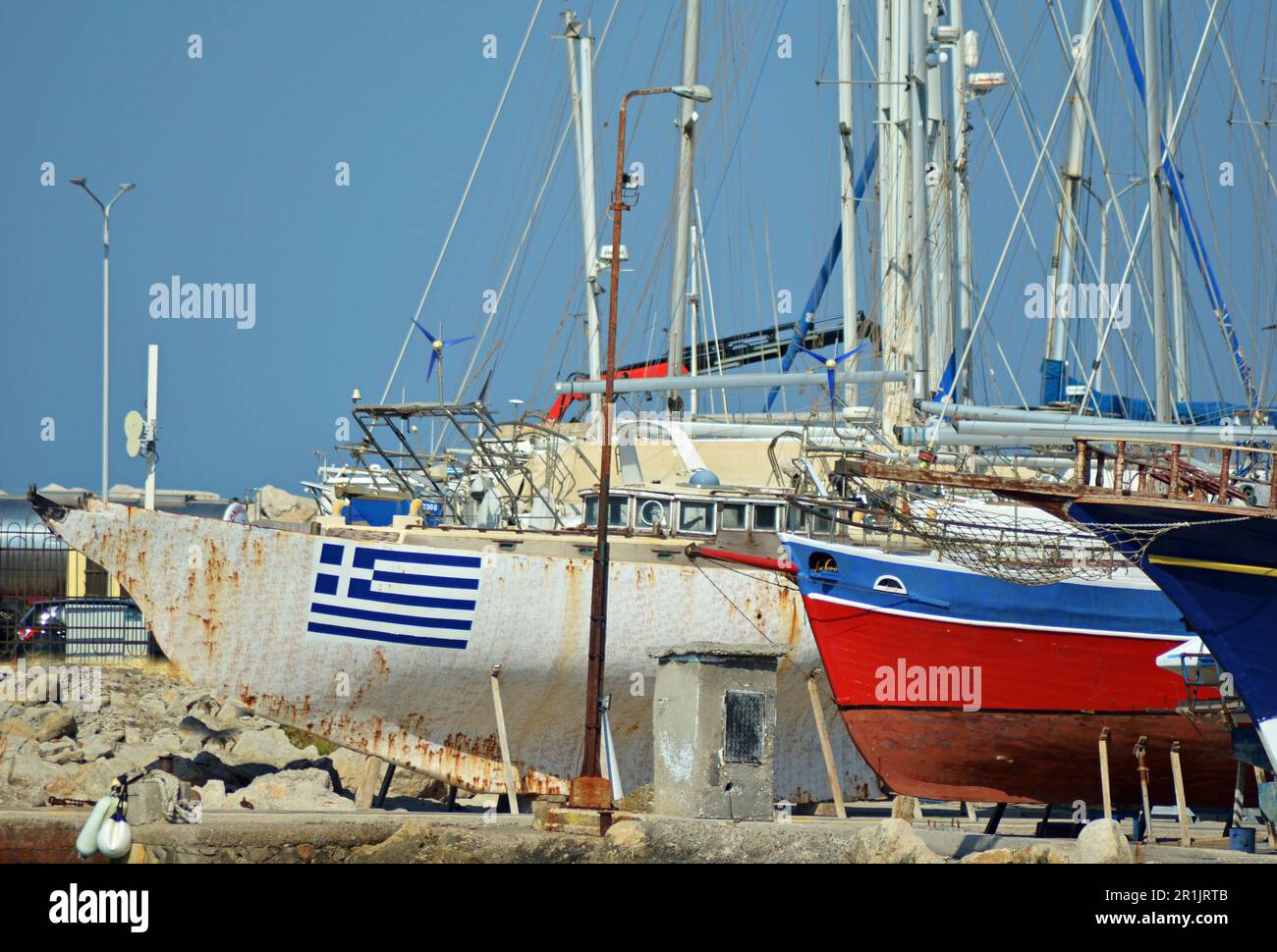 Ship dock, where ships with masts are repaired. One of the white ships has a Greek flag painted on it. The other ship is blue and red. Stock Photo