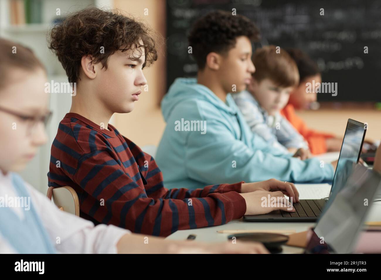 Side view at teenage boy using computer in row in school classroom and ...
