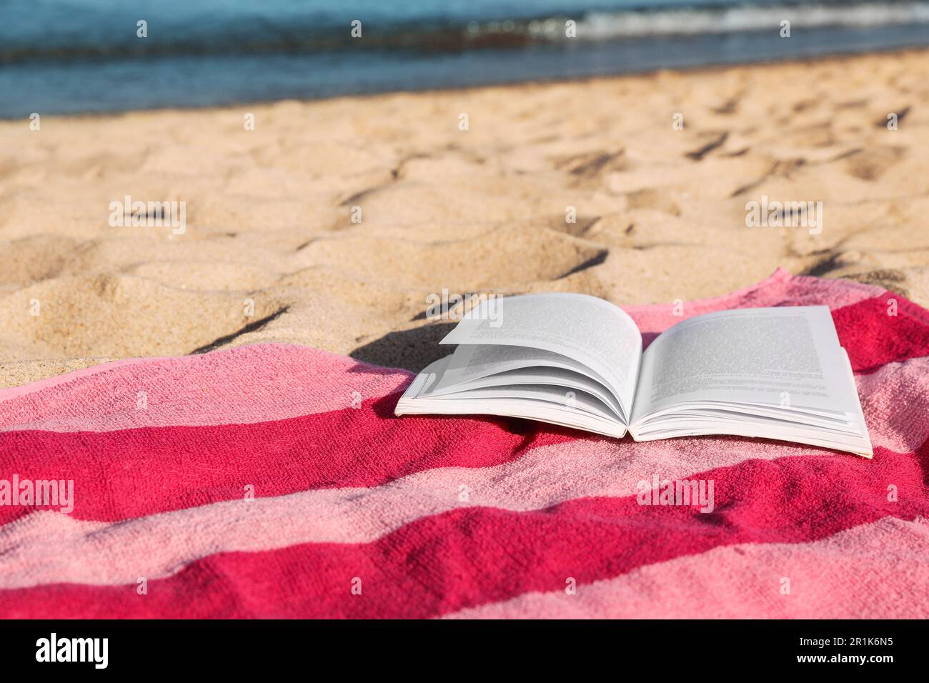 Beach towel and open book on sand near sea, space for text Stock Photo ...