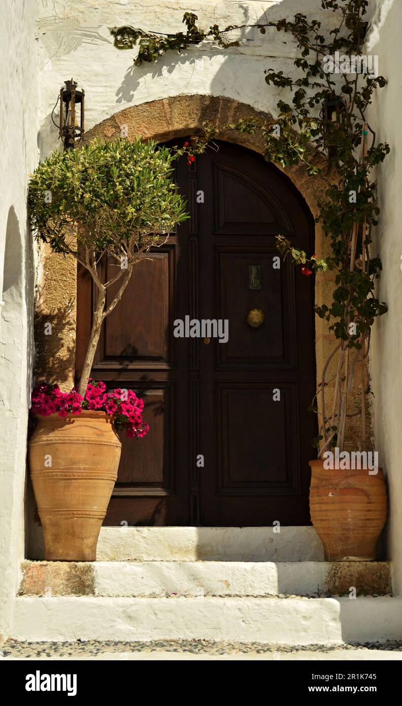Entrance doors of the captain's houses in Lindos, on the island of Rhodes.White walls, wooden arched doors and flowers at the entrance. Stock Photo