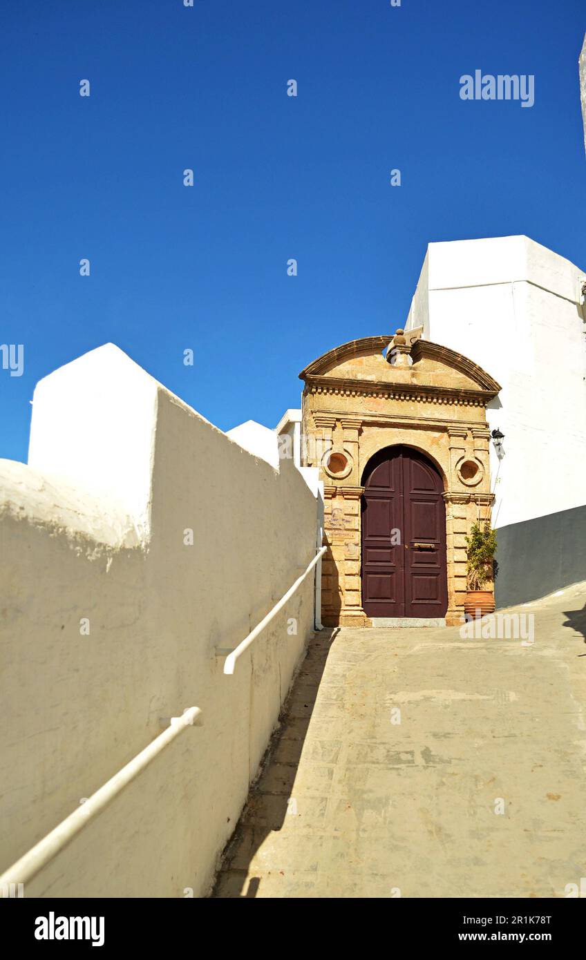 Medieval arched wooden front door to a traditional house in the Greek village of Lindos.Stone arch around the door and the sea on the horizon Stock Photo