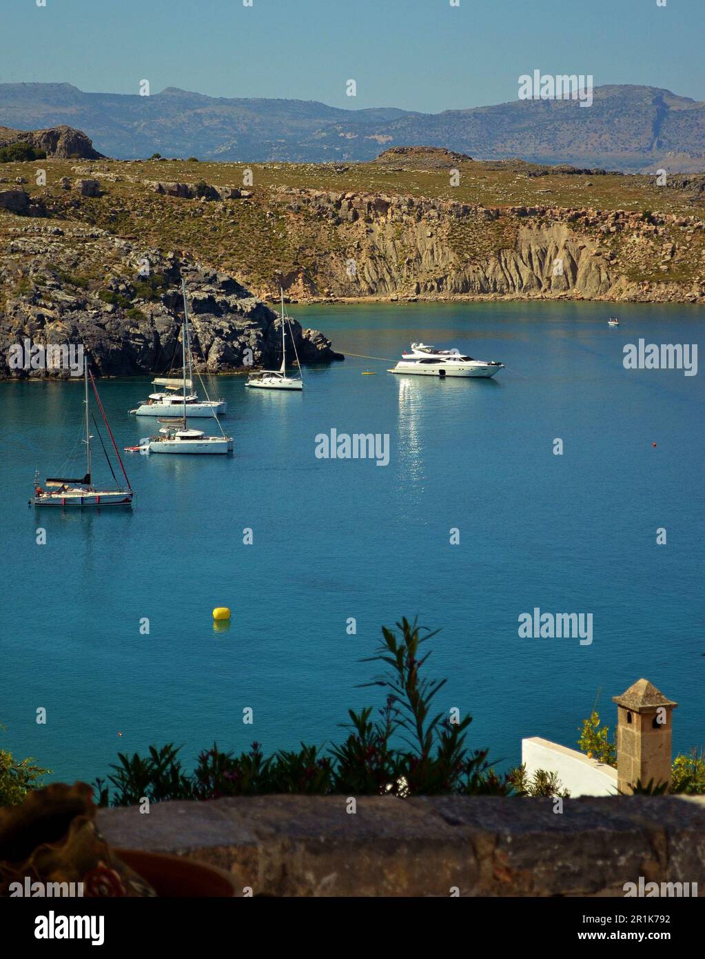Snow-white motor yachts are moored in the bay,near the rocks, in the seaport of Lindos on the island of Rhodes.Mountains are visible in the background Stock Photo