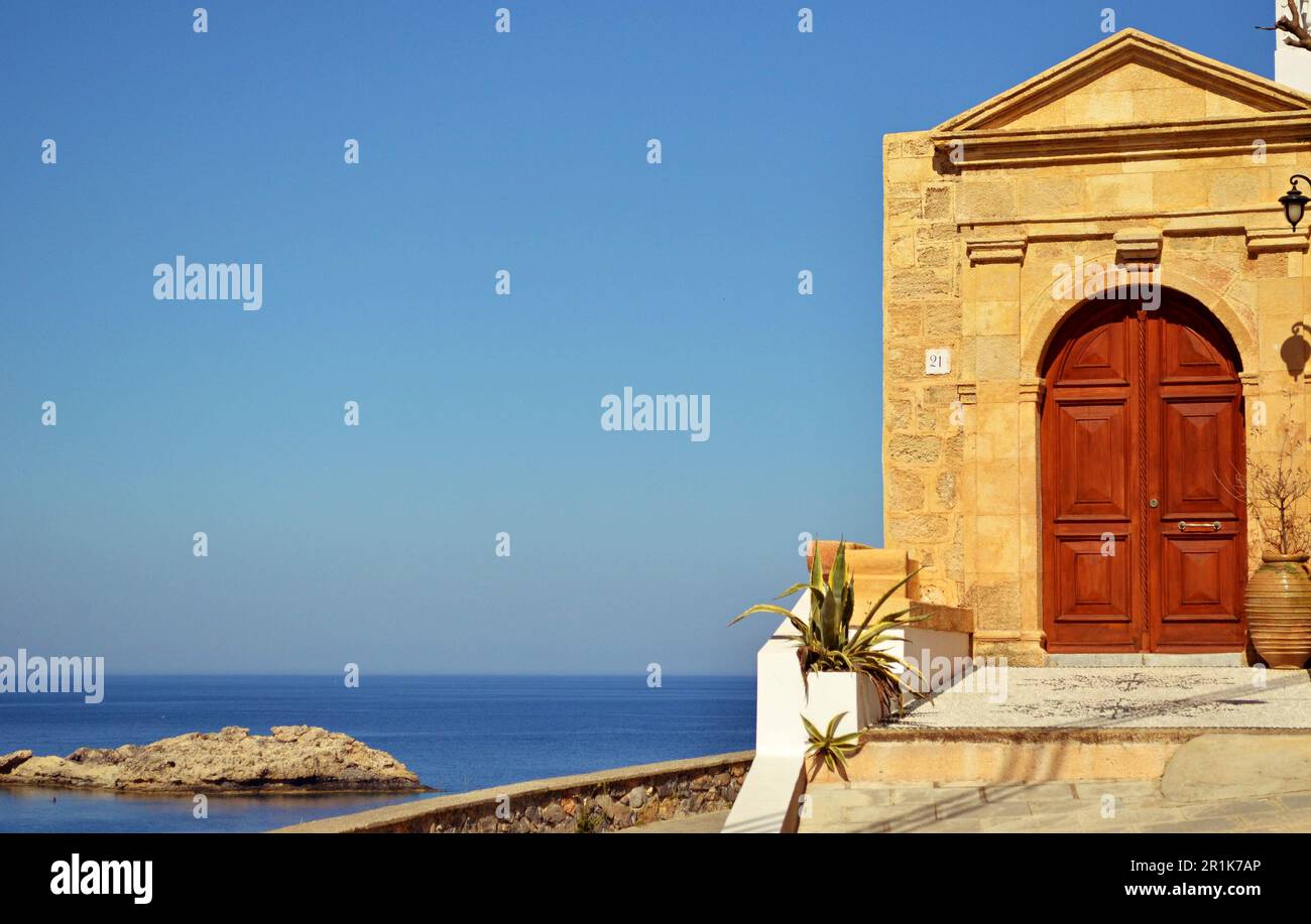 Medieval arched wooden front door to a traditional house in the Greek village of Lindos.Stone arch around the door and the sea on the horizon Stock Photo