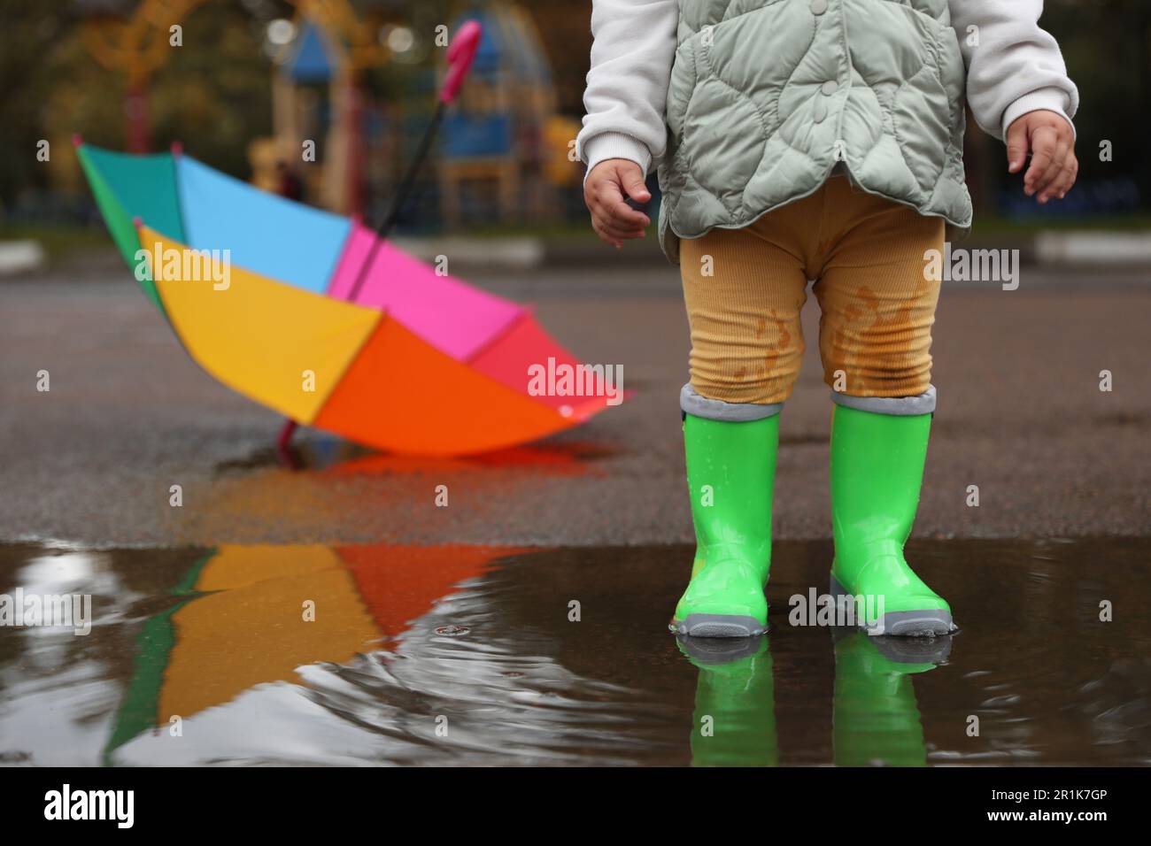 Little girl wearing light green rubber boots standing in puddle ...