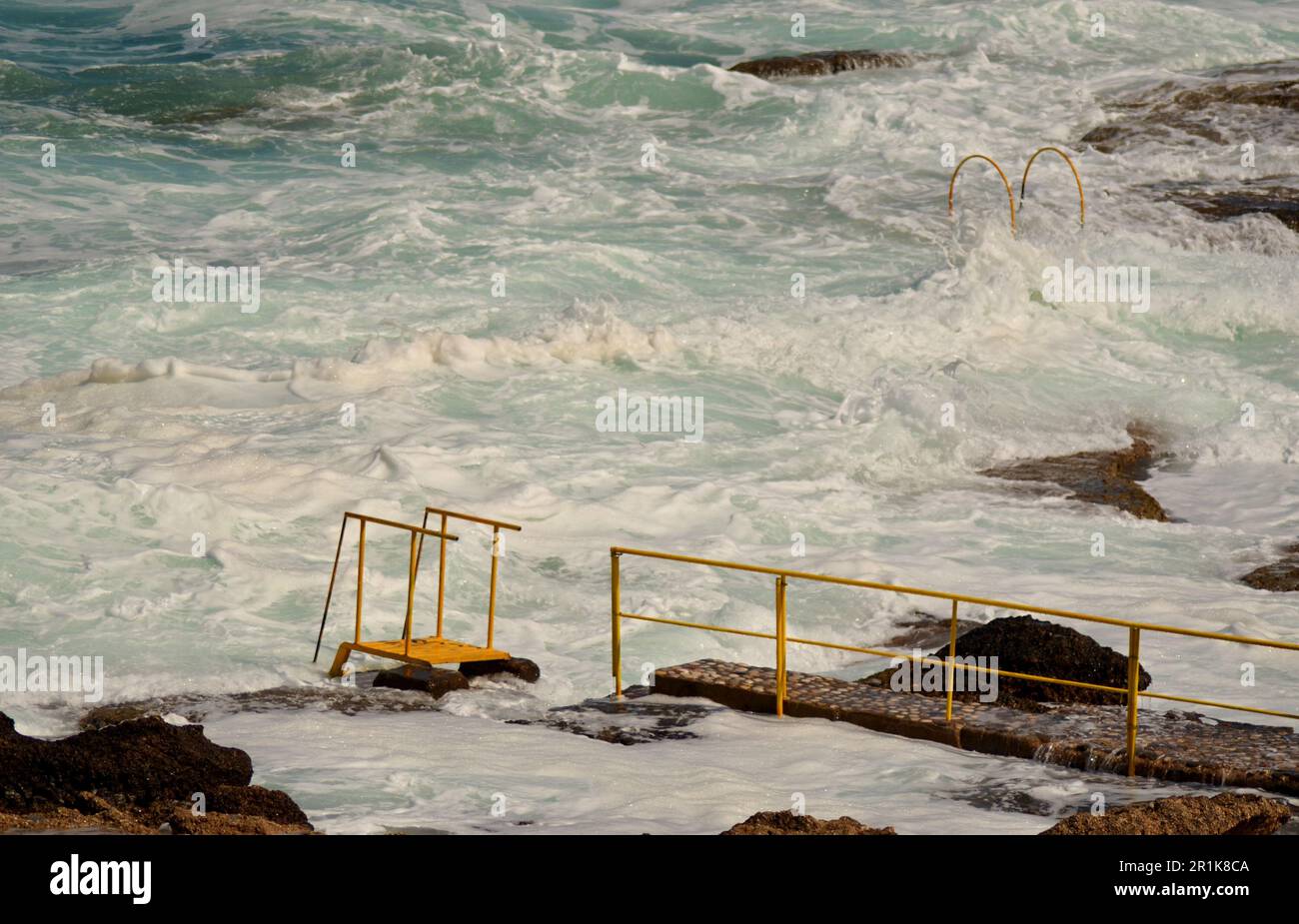 Coast of rocky beach in winter. Strong white sea waves, storm, umbrellas closed. For each umbrella there is a concrete platform. Stock Photo