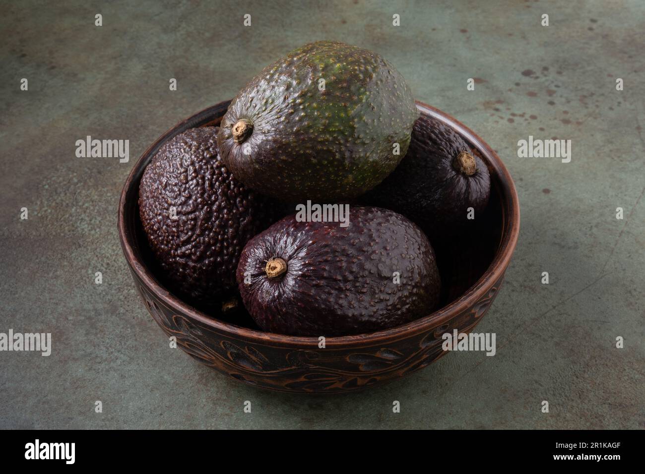 Several ripe avocados lie in a clay bowl. Stock Photo