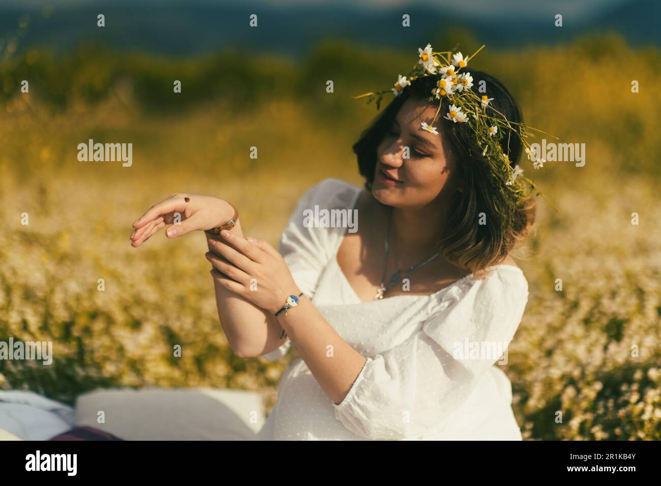 A midsection shot of a pregnant woman holding a ladybug, with a backdrop of blooming flowers and greenery Stock Photo