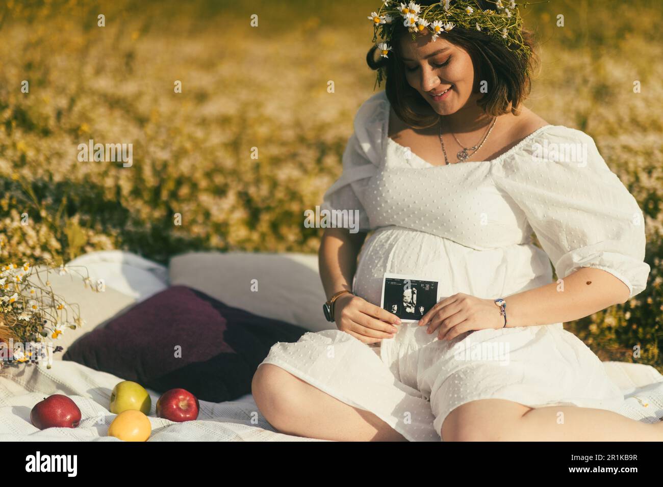 On a white picnic blanket, a pregnant woman proudly displays her baby's