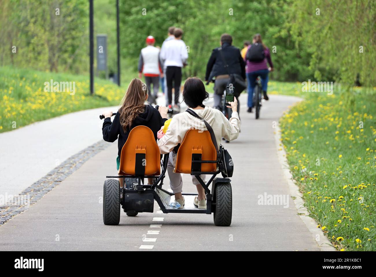 Two girls riding velomobile in a green park. Tandem bike renting for spring or summer leisure Stock Photo
