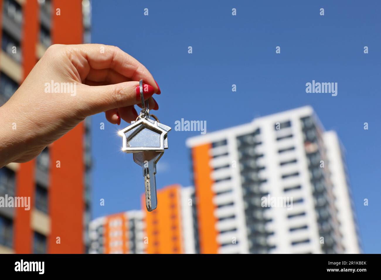 Real estate agent, home keys in female hand on background of new building. Byung apartment or renting property Stock Photo