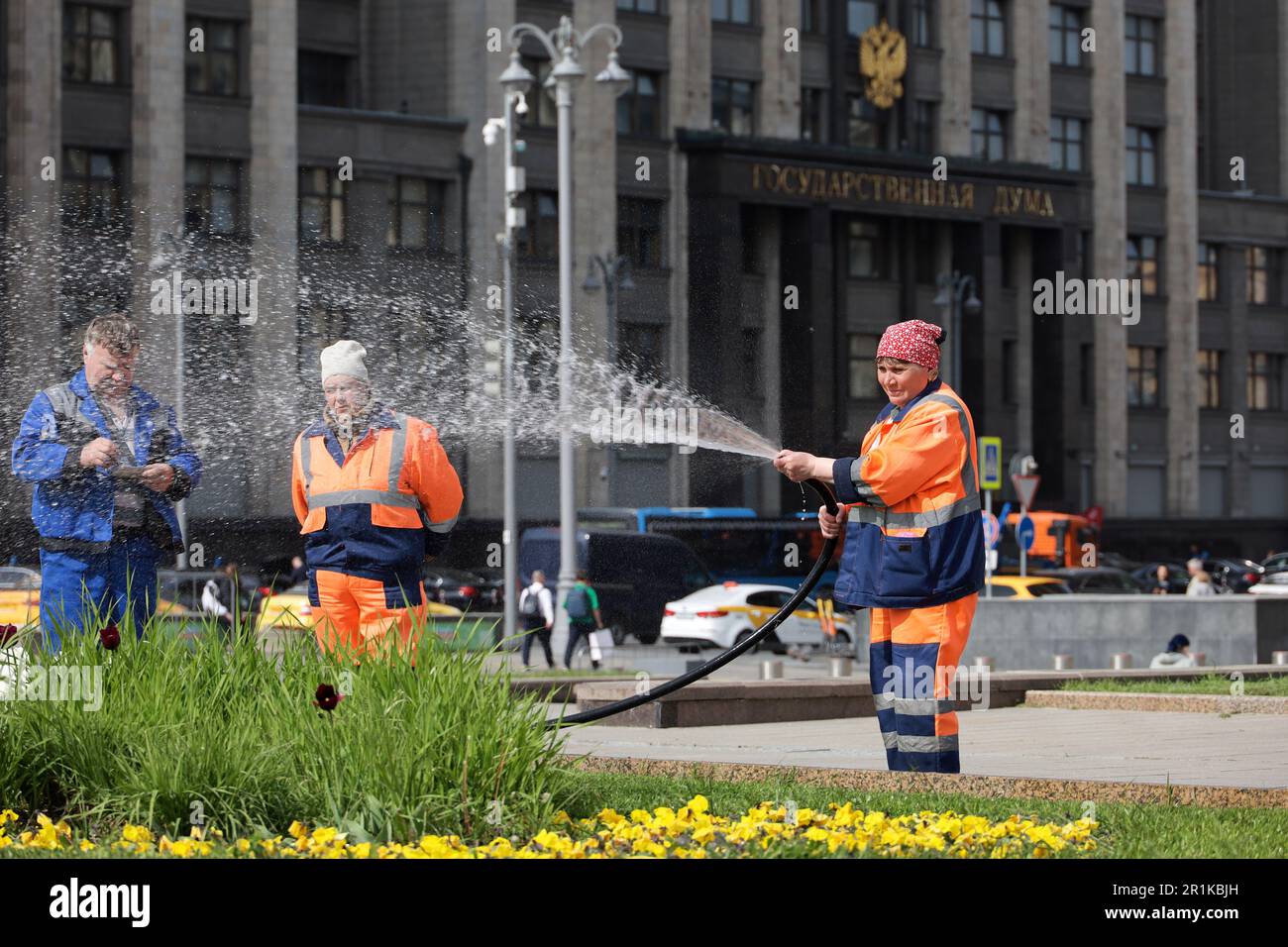 Woman worker watering the lawn and flowers with a hose on Manezhnaya square against State Duma building Stock Photo